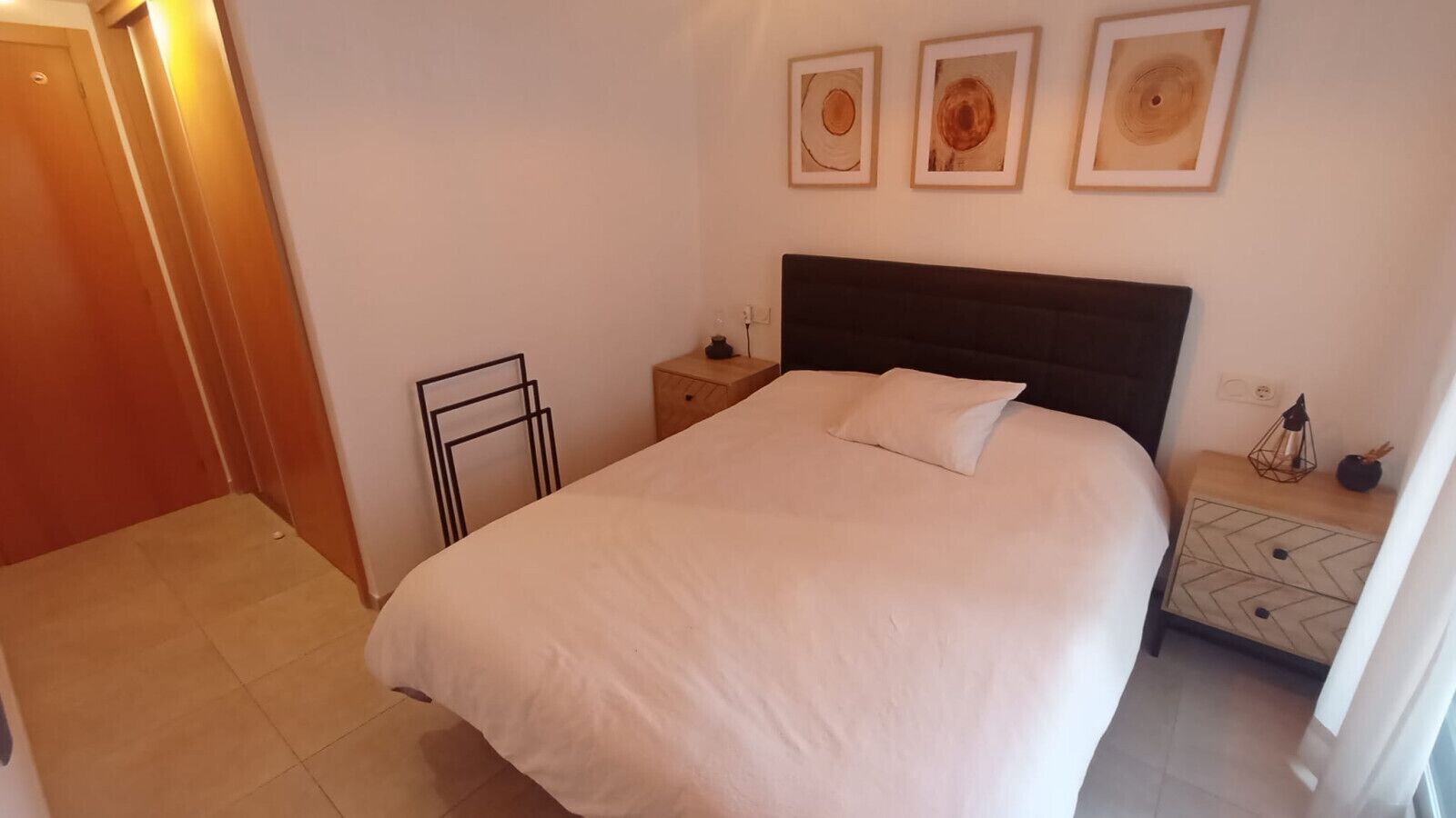 Un dormitorio con una cama grande, una mesita de noche y una estantería en la pared.