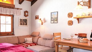 A cozy room with a wooden ceiling, a sofa set, a dining table, and various wall decorations including clocks and framed pictures.