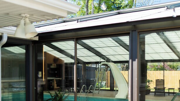 Una piscina techada con tobogán, rodeada de paredes de vidrio y un área de patio.