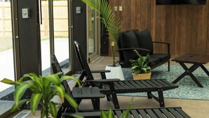 Un espacio interior moderno con una zona de estar que incluye mobiliario de metal negro, plantas en macetas y un televisor de pantalla plana montado en la pared.