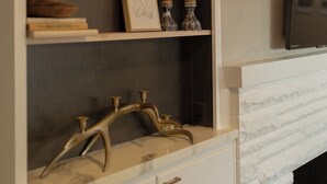 Una sala de estar moderna con chimenea, televisor montado y una estantería decorativa con libros y jarrones.