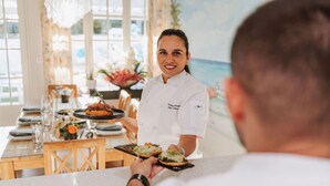 A chef serving dishes in a restaurant with a view of the ocean.