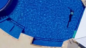 Ein Schwimmbecken mit Whirlpool, umgeben von Liegestühlen und einer gefliesten Terrasse.