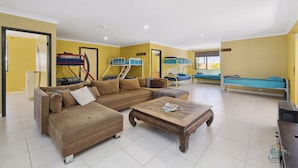 A room with a large brown sectional sofa, a wooden coffee table, and bunk beds with blue bedding. - Studio 37 – Family-Friendly Beachside Retreat (Lancelin)