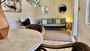 A living room with a round table, wicker chairs, a sofa with patterned cushions, a lamp, and wall-mounted mirrors. - Old Florida bungalow on a tranquil Gulf Island Perfect for Couples or Anglers (Spring Hill)