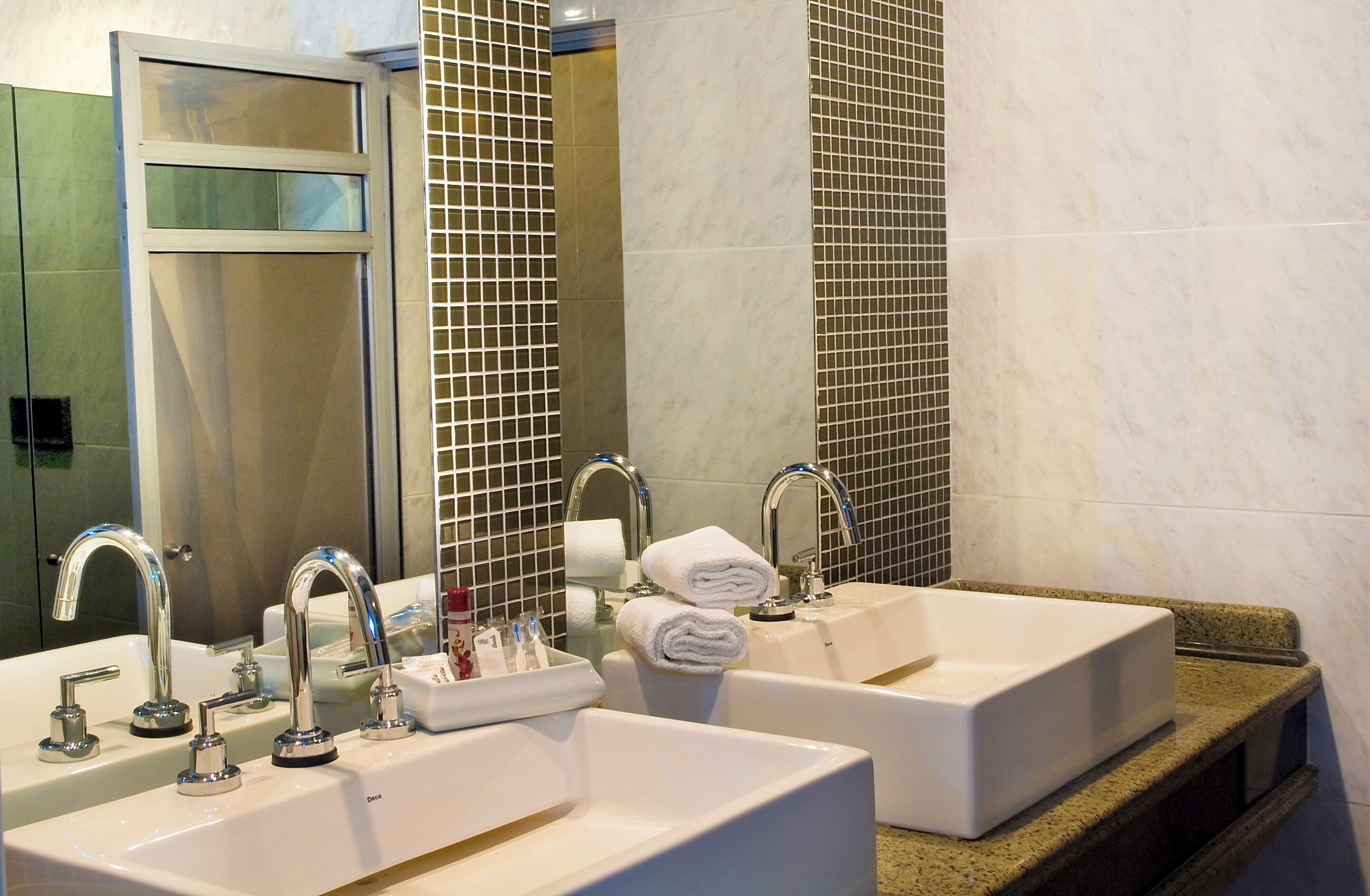 Un baño de hotel con dos lavamanos, cada uno con un espejo, y una pared con azulejos.