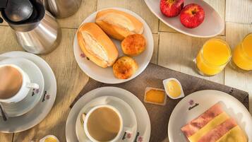 En frukostuppsättning med bröd, äpplen, apelsinjuice, kaffe och smör på ett träbord.