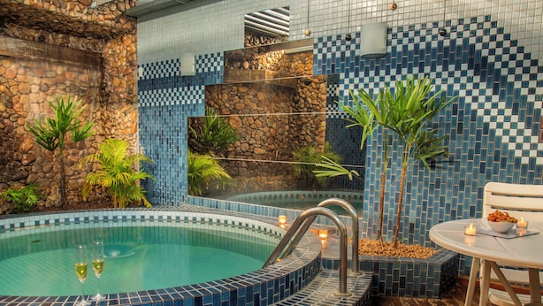 A hot tub with blue mosaic tiles, surrounded by plants and a stone wall. - Motel Chavelle (Sao Jose dos Pinhais)