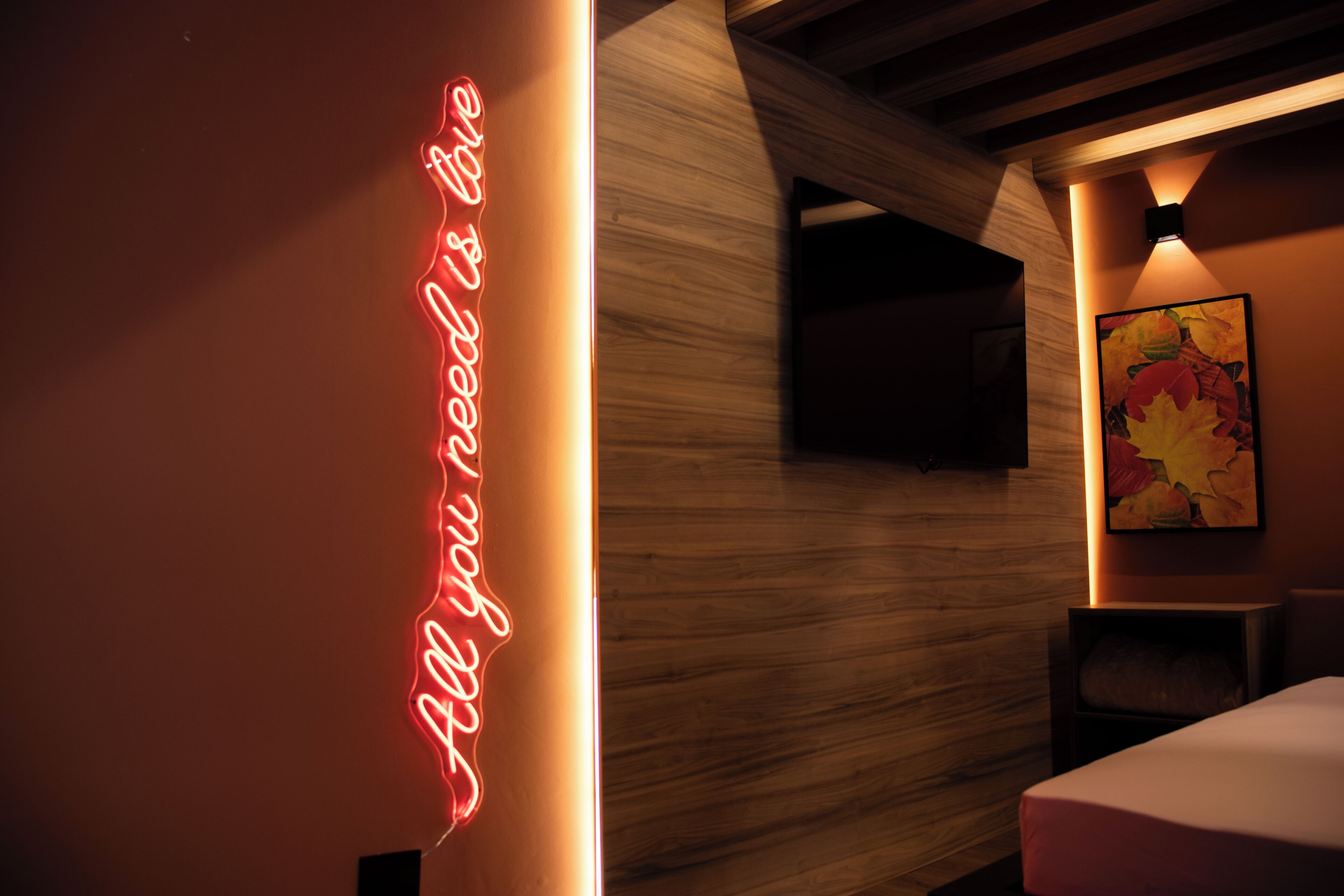 A modern interior with a neon sign, a wooden wall, a painting, and a bed.