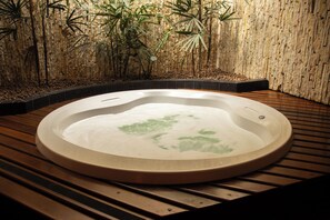A hot tub with a wooden deck and bamboo plants in the background. - Motel Chavelle (Sao Jose dos Pinhais)
