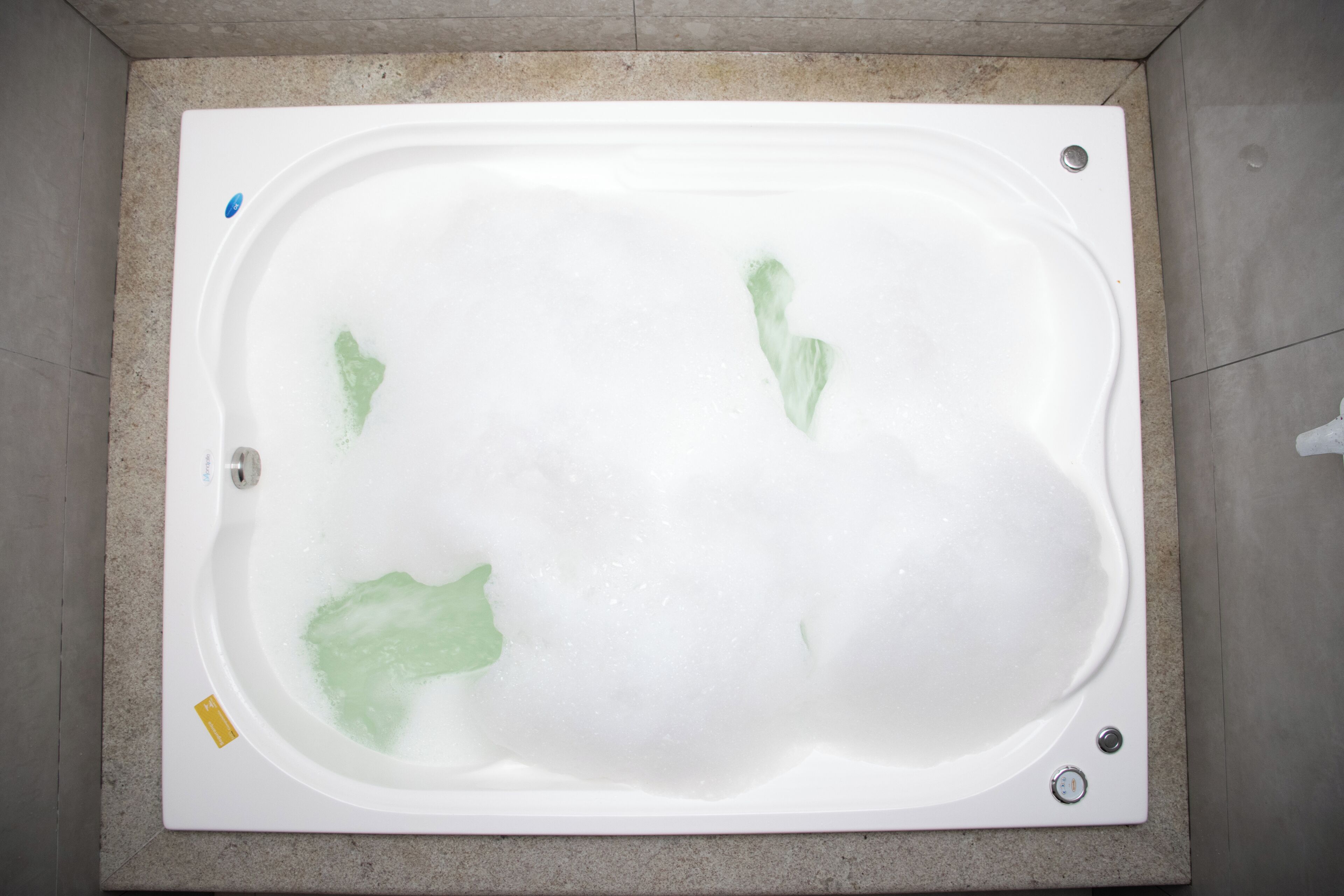 Una bañera rectangular con espuma de jabón visible y un desagüe.