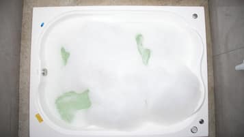 Una bañera rectangular con espuma de jabón visible y un desagüe.