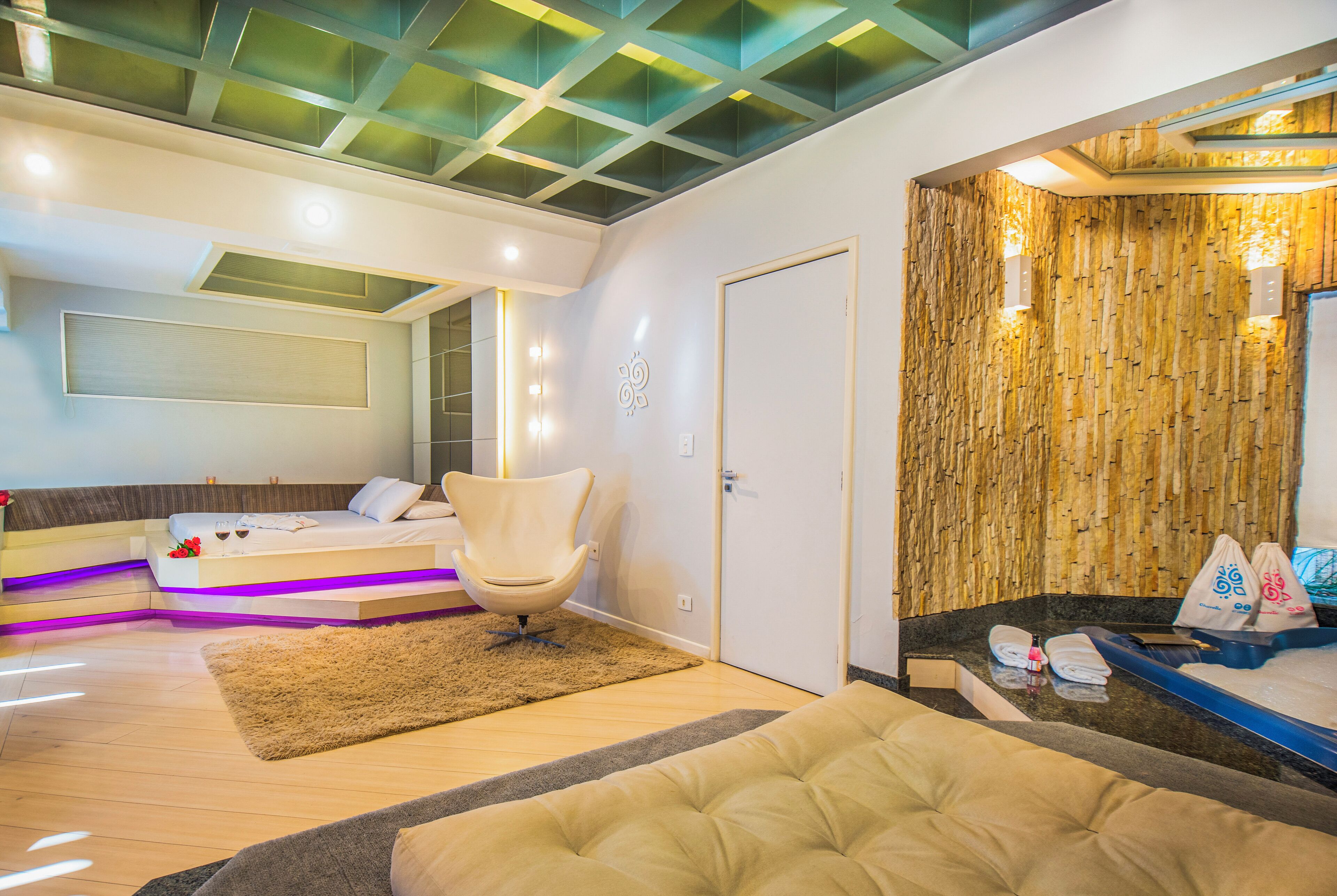 A modern hotel room with a bed, a seating area, a chair, and a bathroom with a wooden wall.
