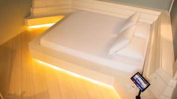 A modern hotel room with a large bed, a bedside table, and a digital device on the nightstand.