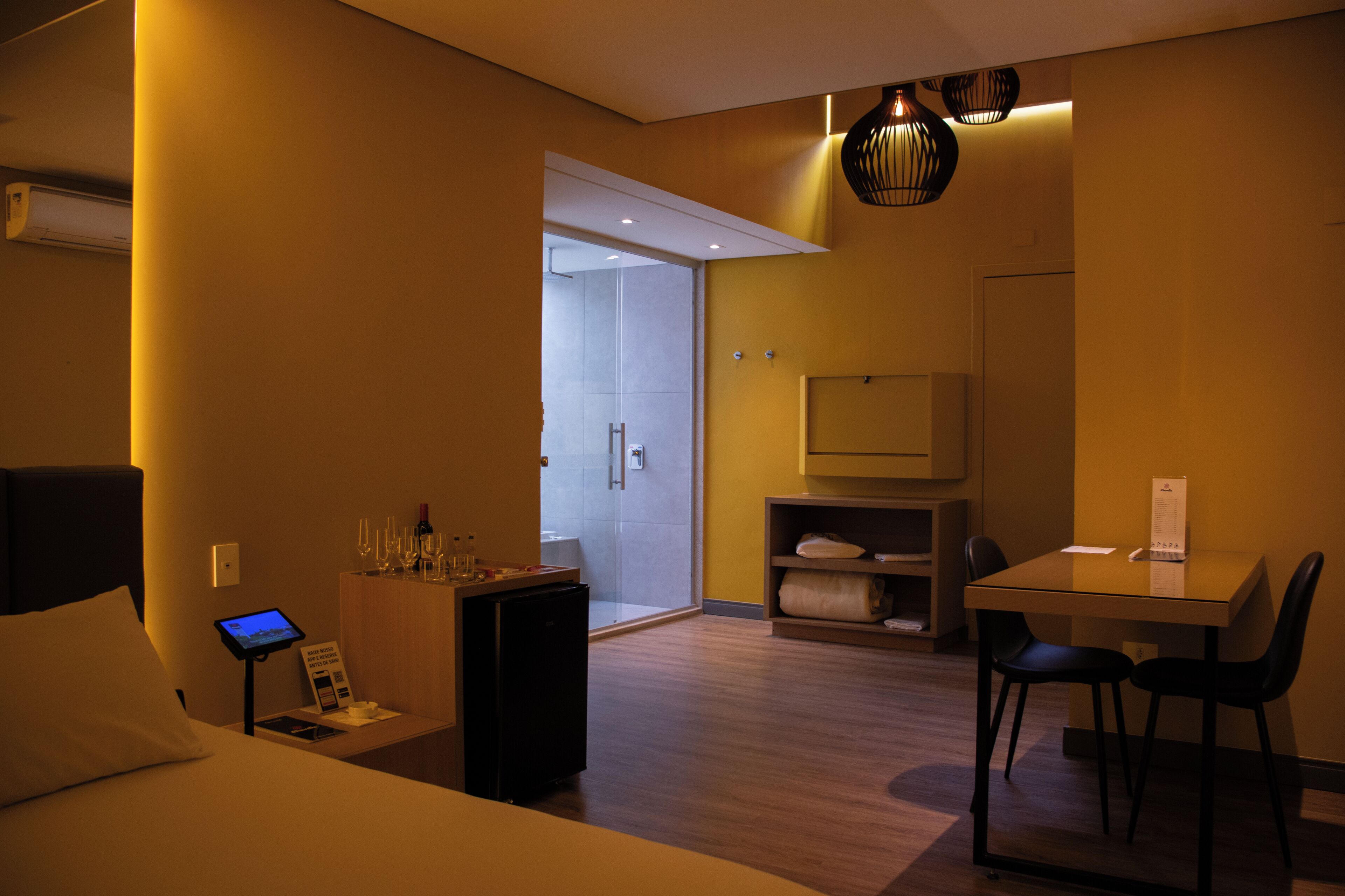 Une chambre d’hôtel comprenant un lit, un bureau avec deux chaises, un petit réfrigérateur, une télévision et une salle de bain visible à travers une porte ouverte.