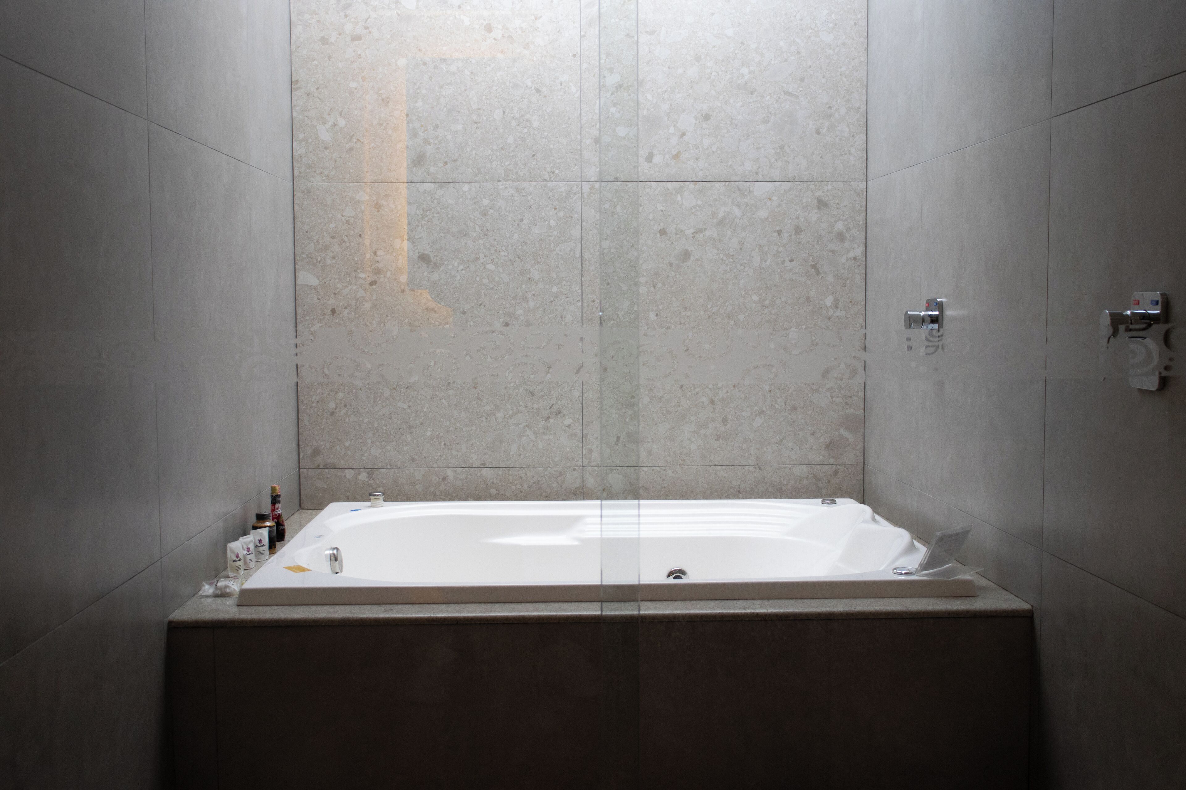 Une salle de bain moderne avec une grande baignoire, des murs carrelés et une petite étagère où sont rangés les produits de toilette.