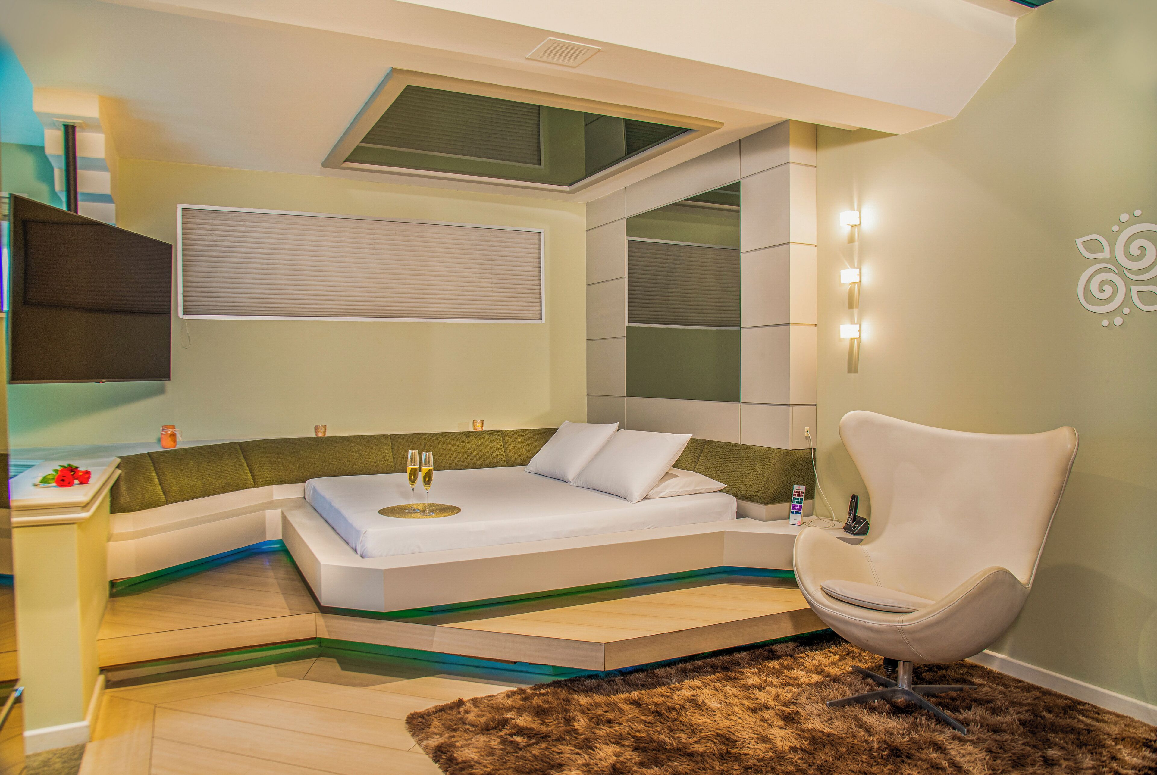 Une chambre à coucher moderne avec un lit aux lignes courbes, une chaise et une petite table sur laquelle sont posés des verres.