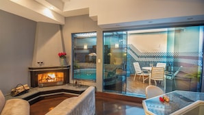 A modern living room with a fireplace, a glass-enclosed patio with outdoor seating, and a view of a pool. - Motel Chavelle (Sao Jose dos Pinhais)