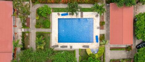 Vue aérienne d’un complexe hôtelier doté d’une piscine centrale, entouré d’une végétation luxuriante et de palmiers.