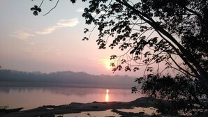 Auringonlasku tyynen vesistön yllä, taustalla kivikkoinen rantaviiva ja edessä vene.