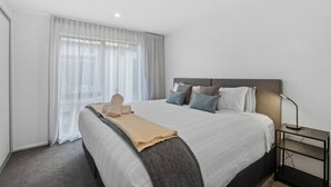 A modern hotel room with a large bed, a bedside table with a lamp, and sheer curtains on the window. - Ride Recover & Rest | Arthurs Point Stay Near Ski & Hot Pools (Queenstown)
