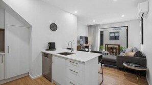 A modern kitchen with a sink, a coffee machine, and a dining area with a sofa and a small table. - Ride Recover & Rest | Arthurs Point Stay Near Ski & Hot Pools (Queenstown)