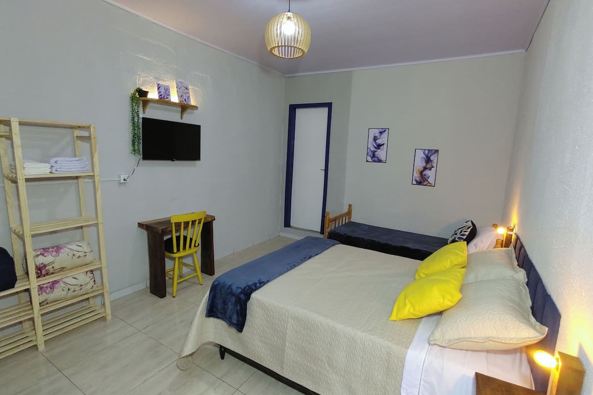 A bedroom with a bed, a desk, a chair, a TV, and a wardrobe.
