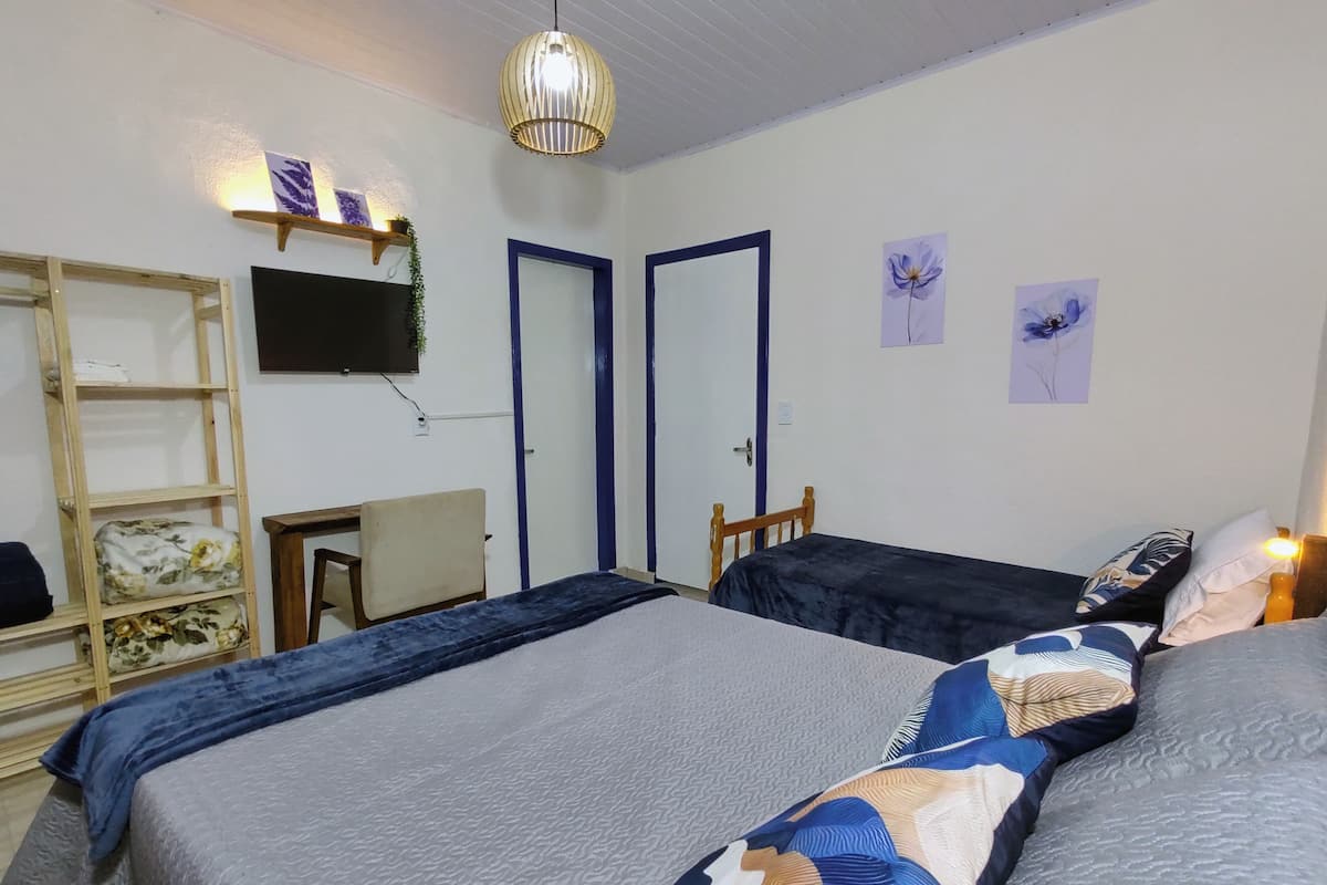 A bedroom with two beds, a desk, a chair, a TV, and a shelf with decorative items.