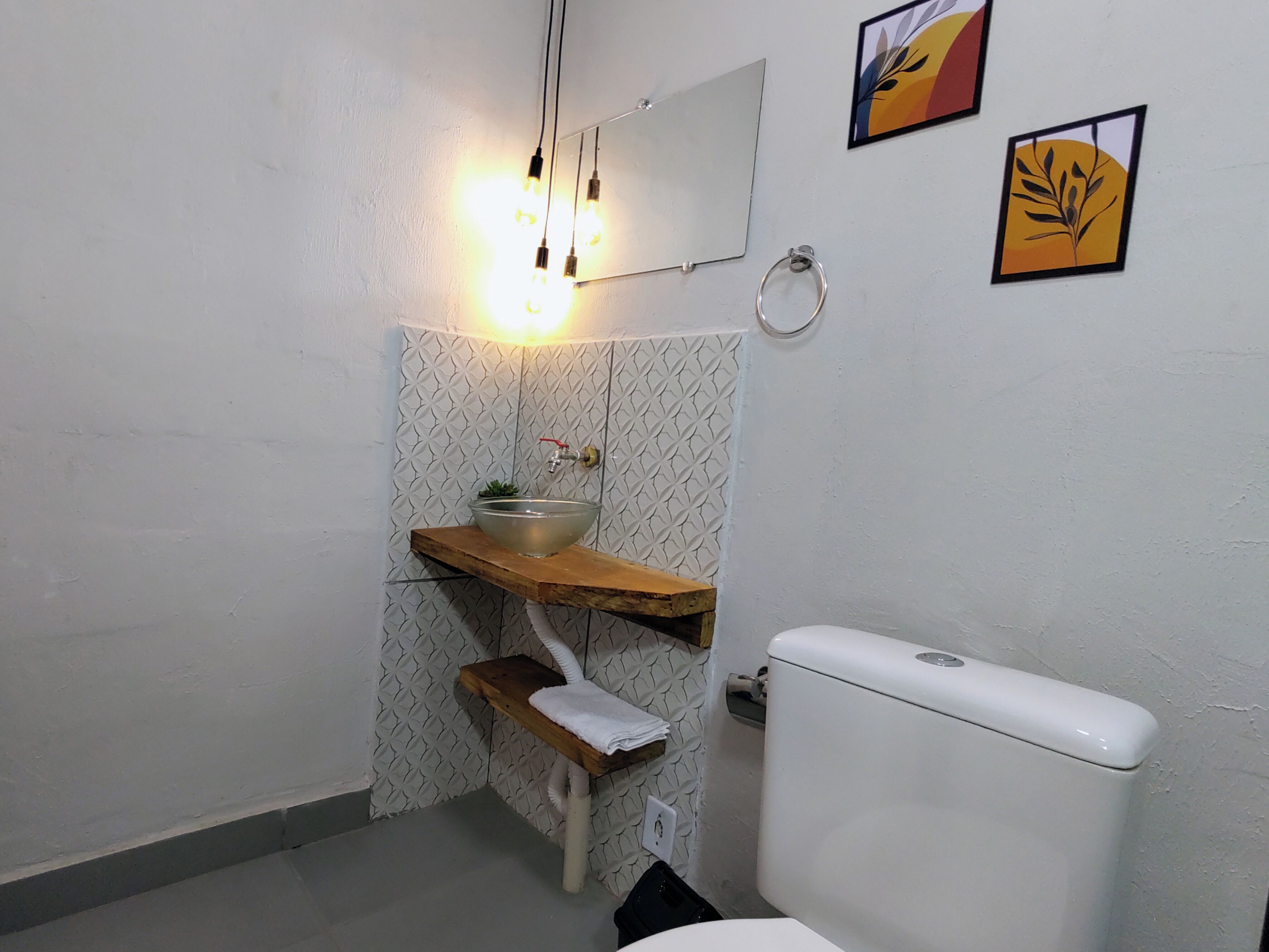 A bathroom with a white toilet, a wooden shelf with a glass bowl sink, a towel rack, and a wall-mounted mirror.