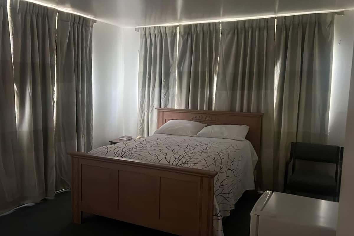 A bedroom with a bed, curtains, a bedside table, and a chair.