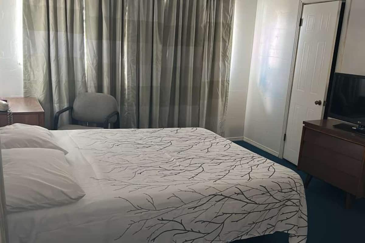 A hotel room with a bed, a chair, a television on a dresser, and a door.