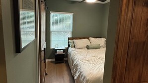Ein Schlafzimmer mit einem Bett, einem Deckenventilator, einem Fenster mit Jalousien und einer Tür.