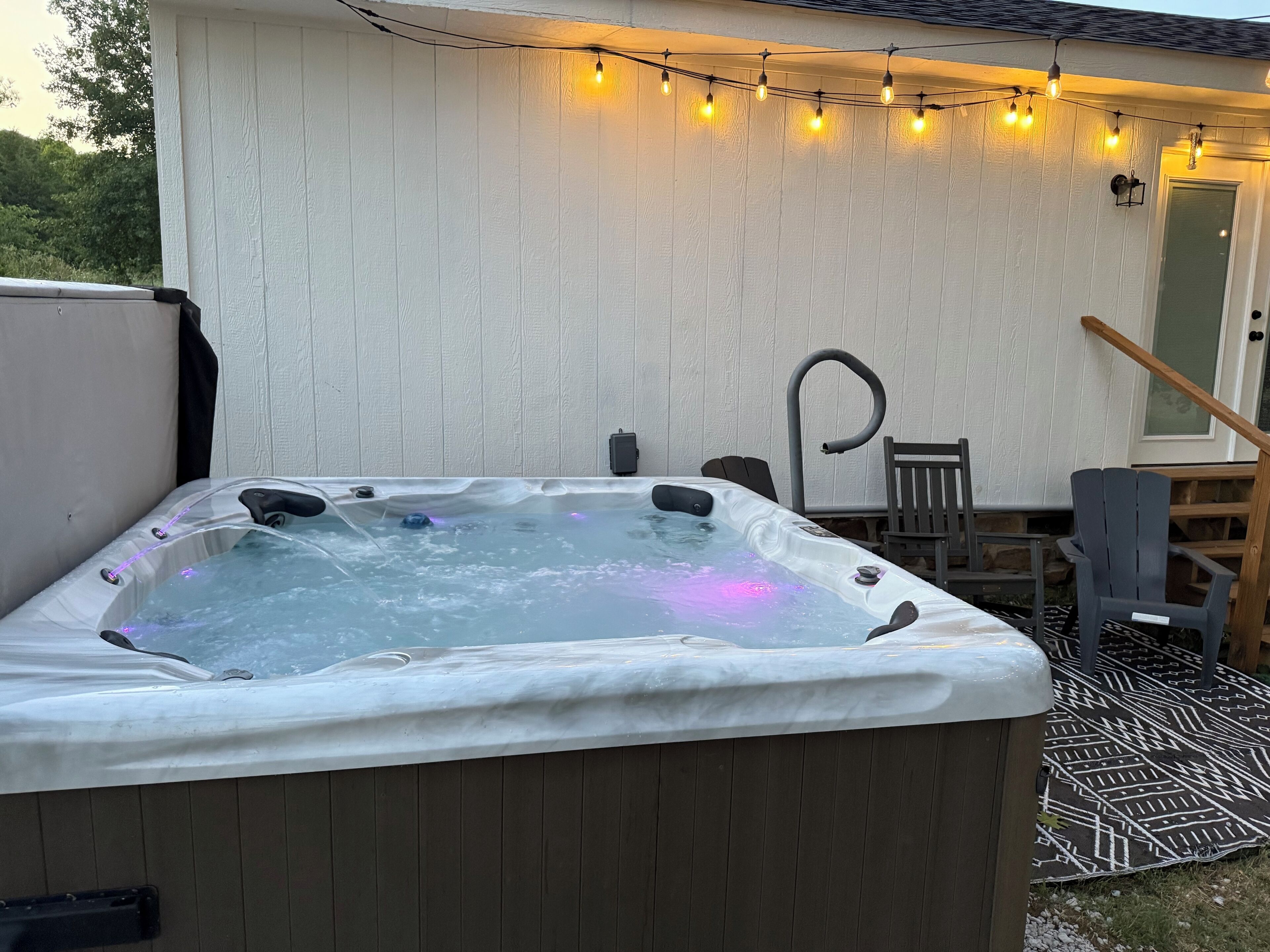 A hot tub with a wooden deck, a chair, and string lights.