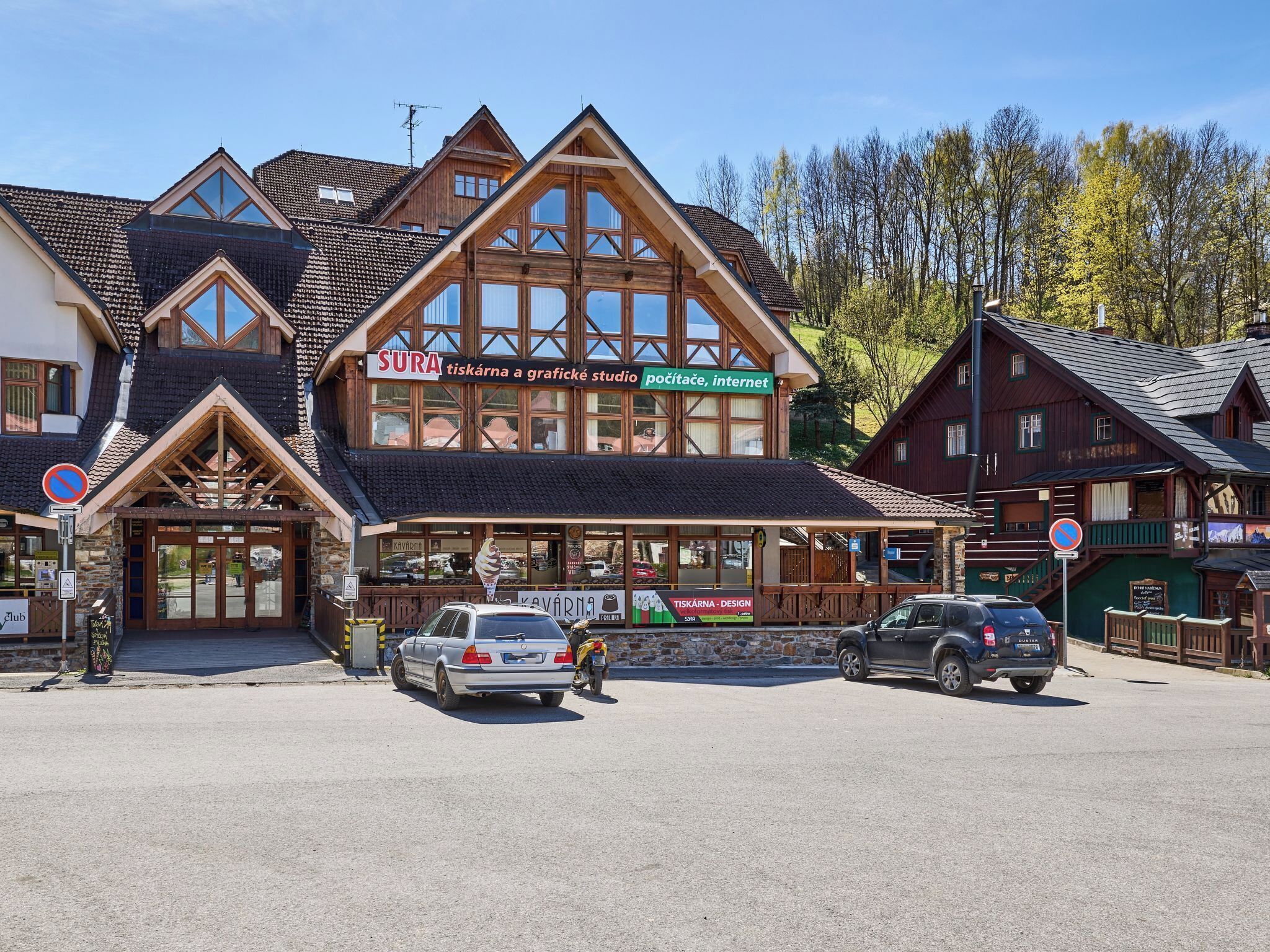 Ein traditionelles Holzhaus mit einem Schild für 'SURA' und einem geparkten Auto davor.