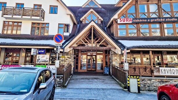 A building with a ski lodge entrance, a sign for 'SURA' and 'KAVARN', and an ATM on the left.