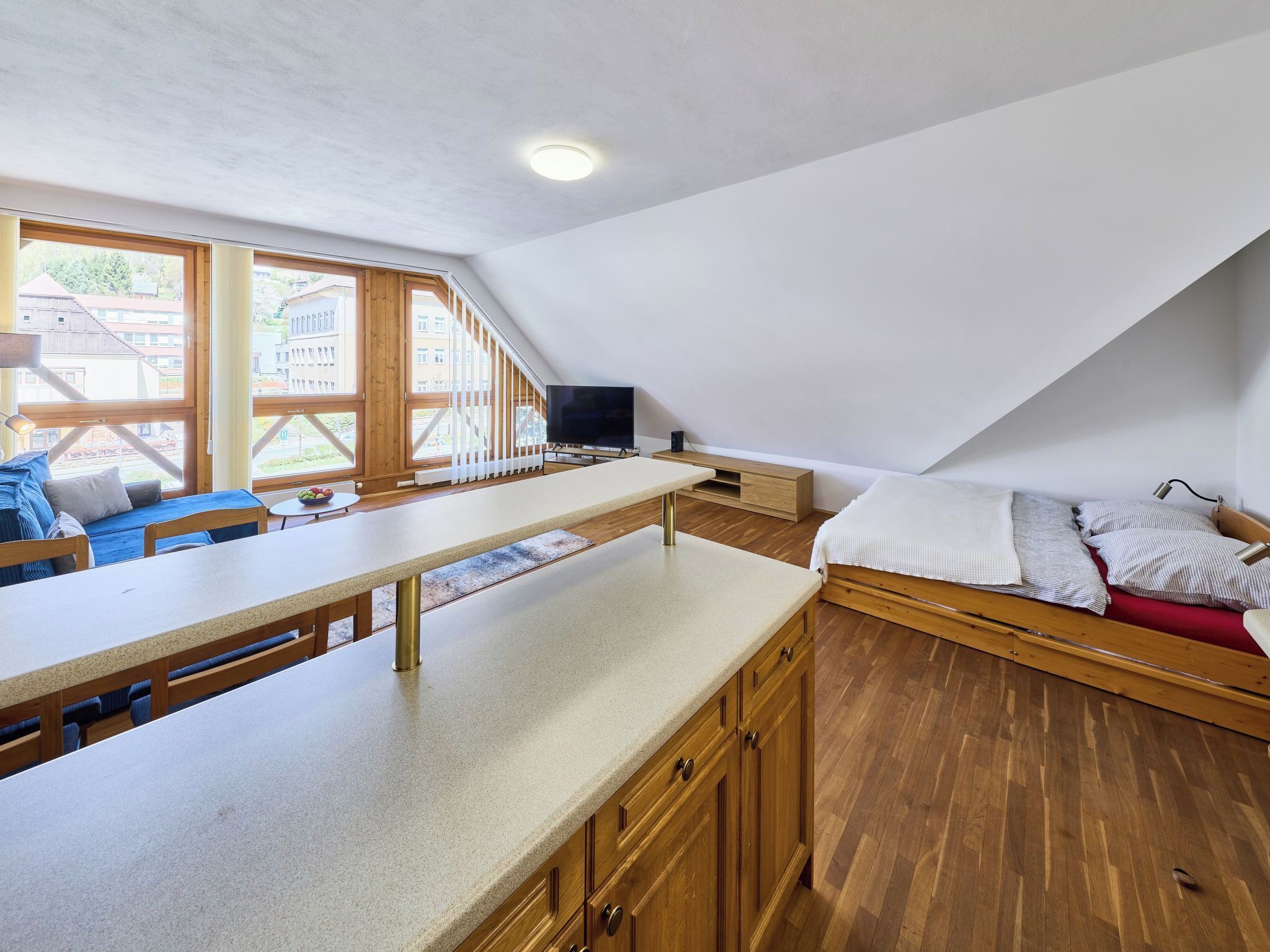 Ein modernes Schlafzimmer im Loft-Stil mit großem Fenster, Bett, Schreibtisch und Fernseher.