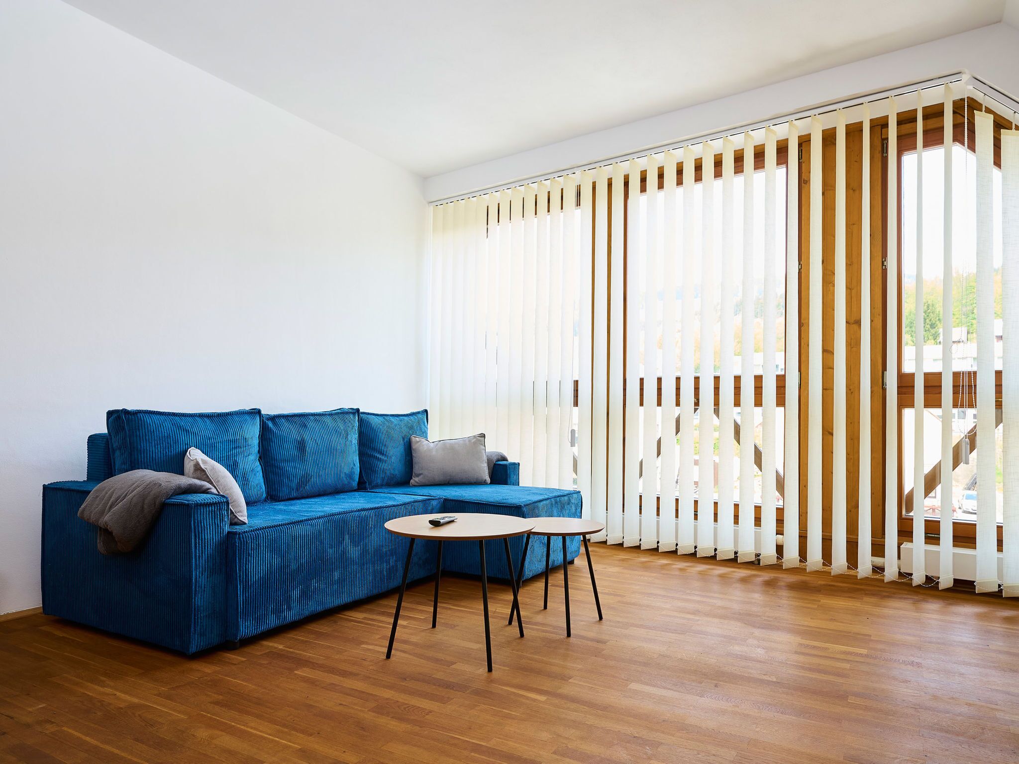 Un soggiorno moderno con un divano blu, un tavolino rotondo e un'ampia finestra con tende verticali.