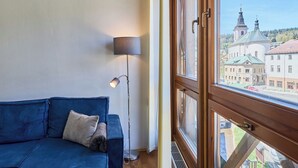 A room with a blue sofa, a floor lamp, and a window with a view of buildings and a church steeple.