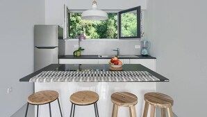 A modern kitchen with a central island, bar stools, a refrigerator, a sink, a window with a view of greenery, and a pendant light. - Awesome home in Fazana (Fazana)