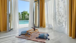 A room with a large sliding glass door leading to a pool, a wooden coffee table with a wine bottle, and two blue pillows on a striped rug. - Awesome home in Fazana (Fazana)