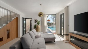 A modern living room with a grey sectional sofa, a flat-screen TV, and a view of a swimming pool. - Luxurious home in Trget (Trget)