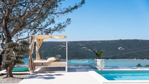 A private pool area with a canopy seating area overlooking a clear blue lake and hills. - Luxurious home in Trget (Trget)