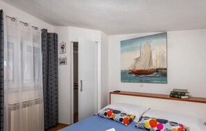 A bedroom with a bed, colorful pillows, a painting of a sailboat, a window with sheer curtains, and a door leading to a closet. - Lovely home in Selce with WiFi (Selce)