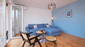 Ein modernes Wohnzimmer mit einem blauen Sofa, zwei runden Tischen, einer Stehlampe und einem großen Fenster.