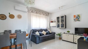 Un soggiorno moderno con un divano grigio, un tavolo da pranzo con sedie, una TV e un mobile bar con ante in vetro.