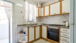 Una cucina compatta con mobili bianchi, un piano di lavoro in granito, un fornello a gas e un frigorifero.
