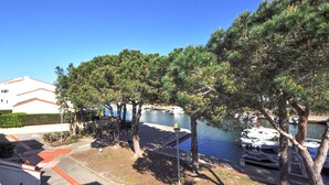 A marina with boats docked, a white building with a red roof, and trees with pine cones. - Beach front home in Saint-Cyprien Plage (Saint-Cyprien Plage)