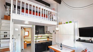 A compact studio apartment with a kitchenette, a dining area, and a loft bedroom with a balcony. - Beach front home in Saint-Cyprien Plage (Saint-Cyprien Plage)