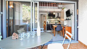 A patio with a round table, chairs, and a glass door leading to a kitchen area. - Beach front home in Saint-Cyprien Plage (Saint-Cyprien Plage)
