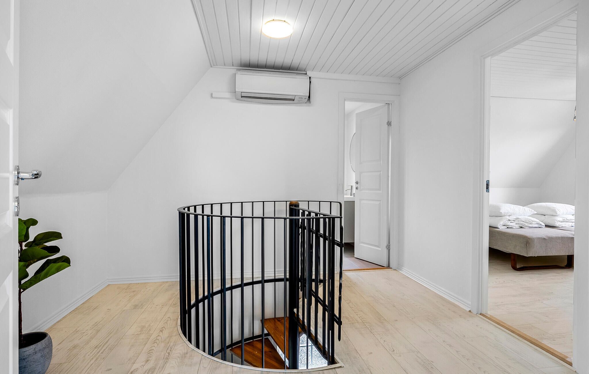 A room with a spiral staircase, a ceiling-mounted air conditioner, and a bed in the adjacent room.
